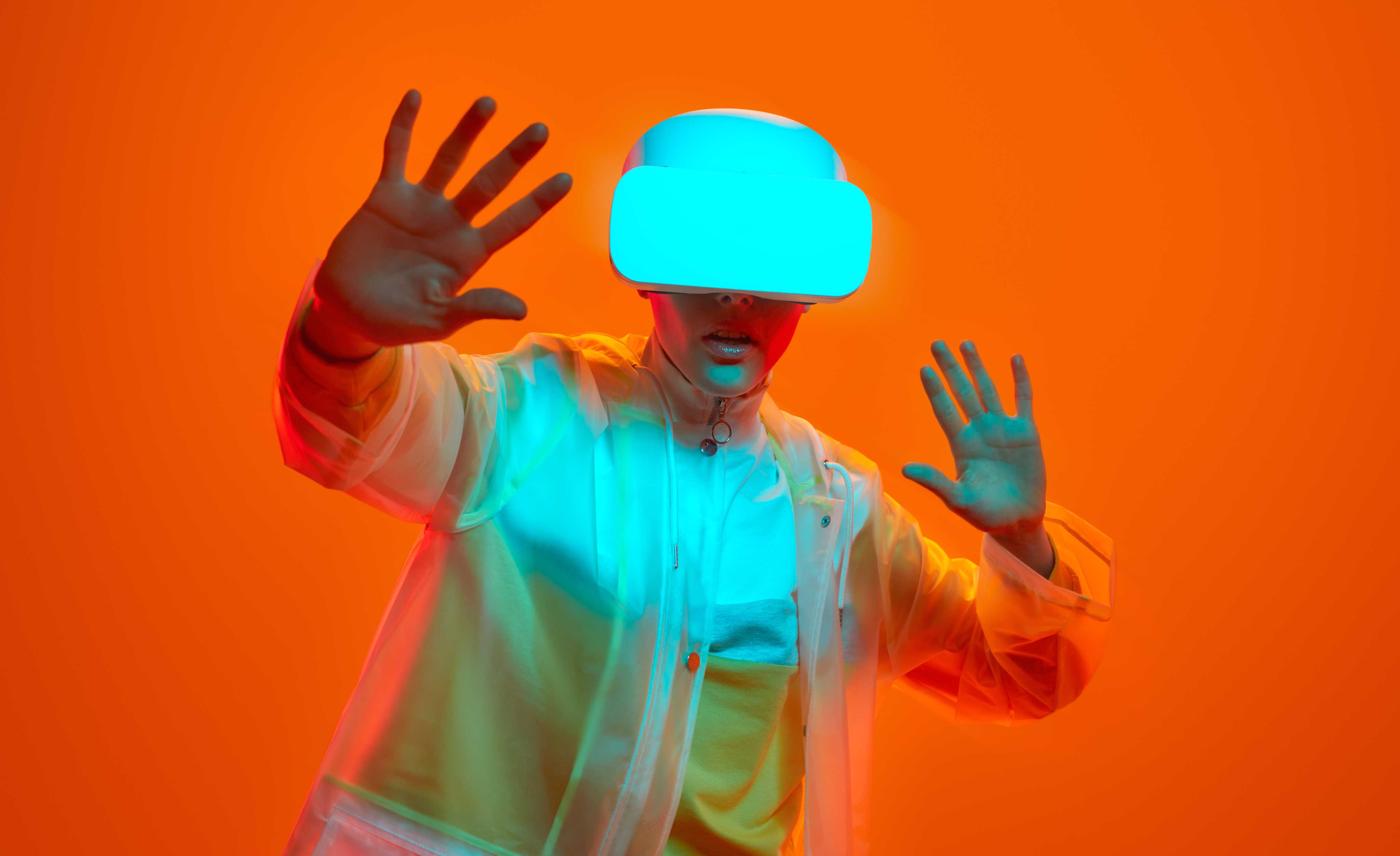 Person wearing VR goggles, raising hands against an orange background.